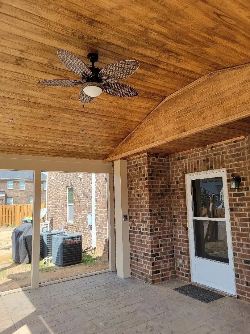 Covered brick patio with wood ceiling, ceiling fan, and white screen door beside a brick wall