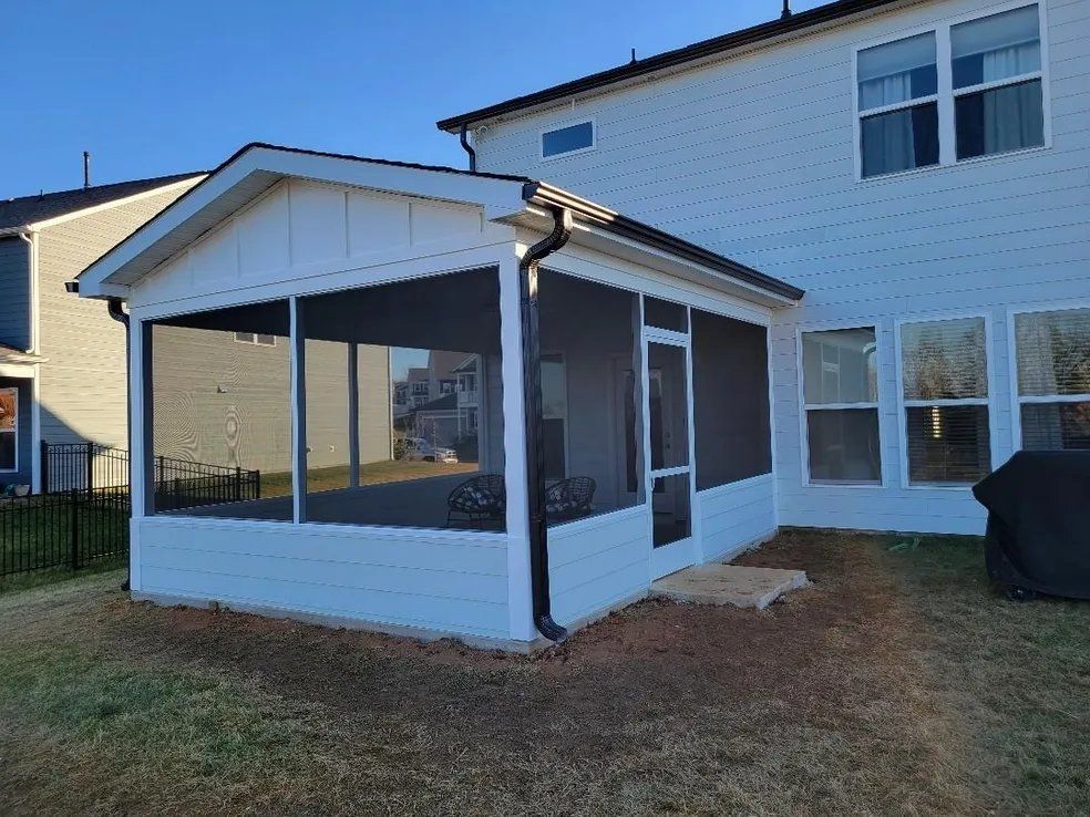 Covered backyard patio beside a white house with screened windows and a sloped roof