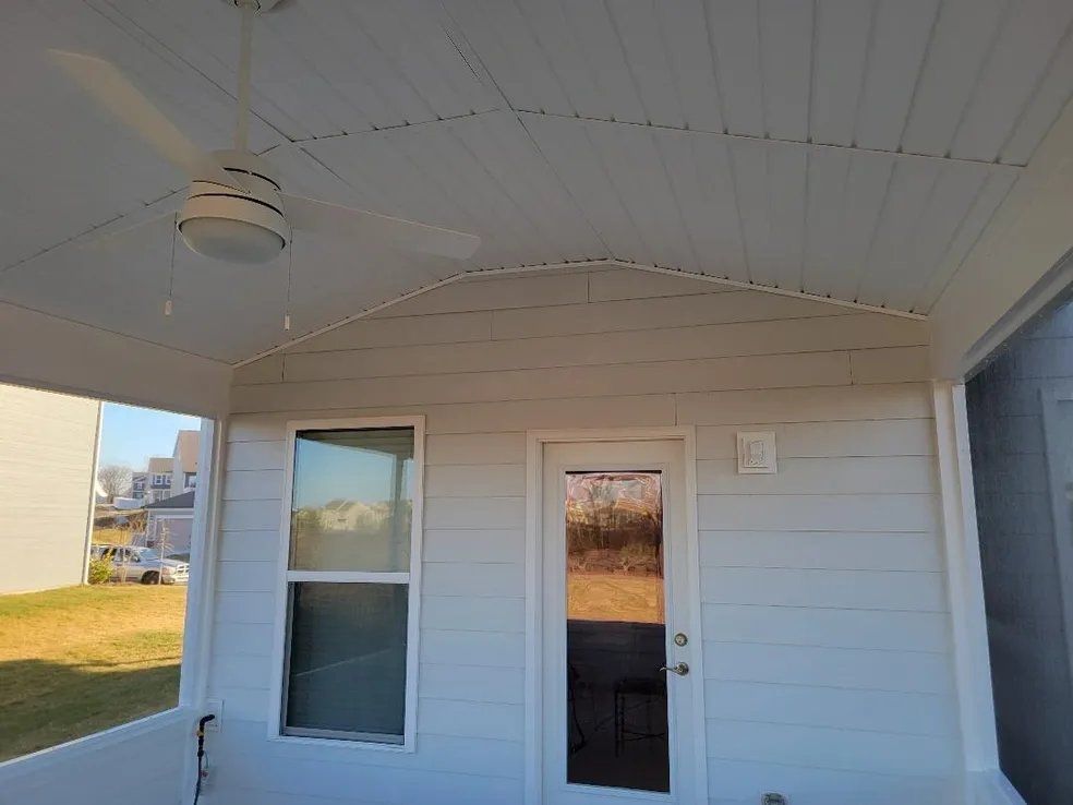 Covered porch with white siding, a ceiling fan, two windows, and a glass door.