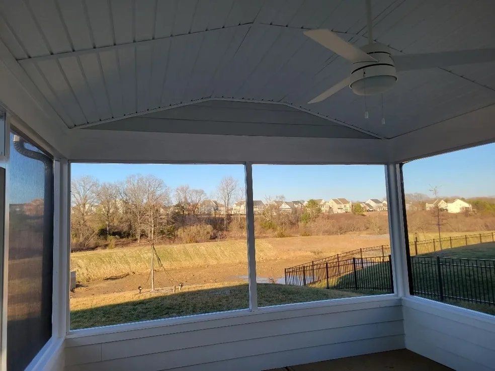Covered porch overlooking a grassy field and trees, with white railings and ceiling fan