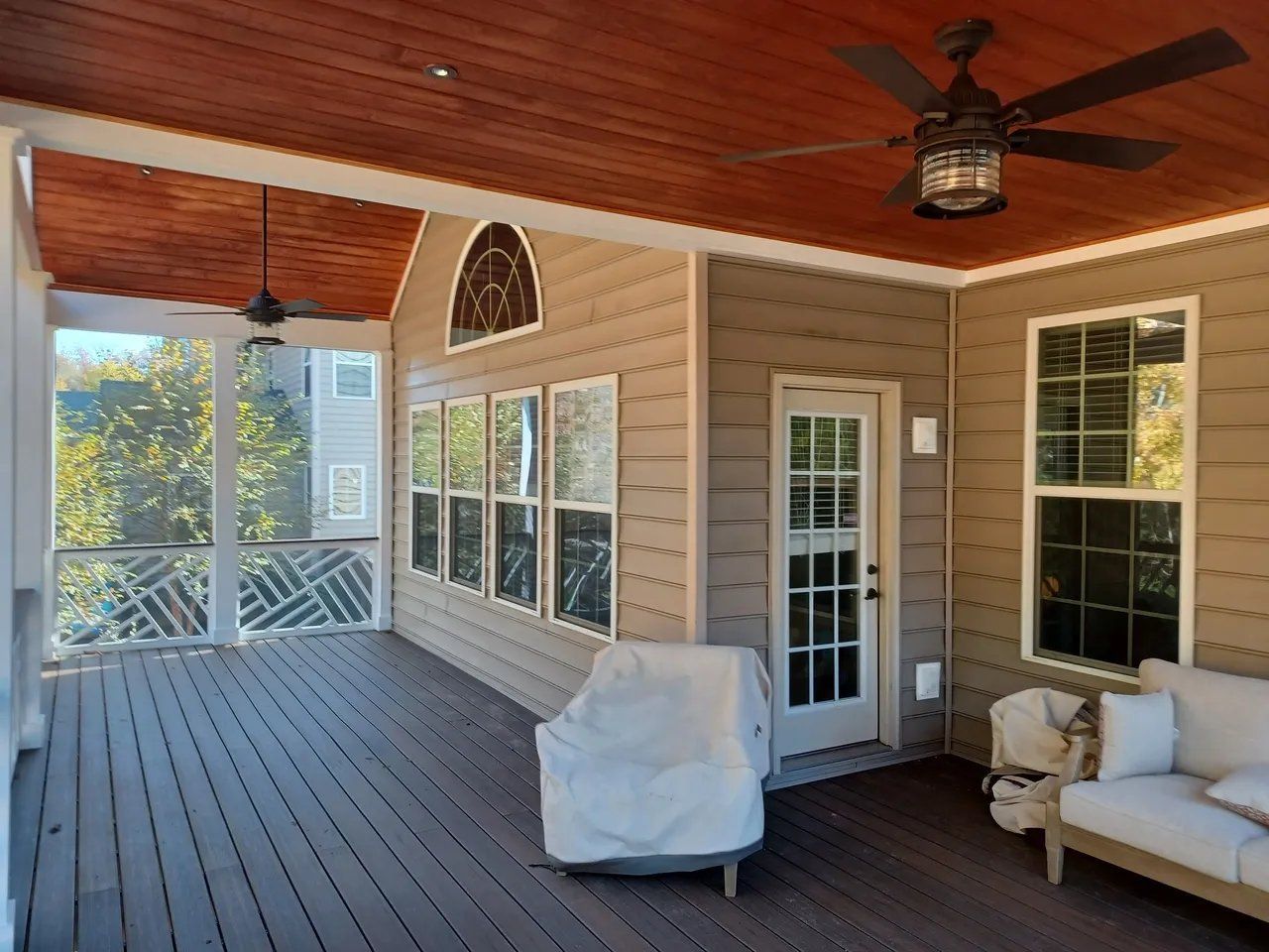 Covered porch with wood ceiling, ceiling fan, white siding, and wicker seating overlooking greenery