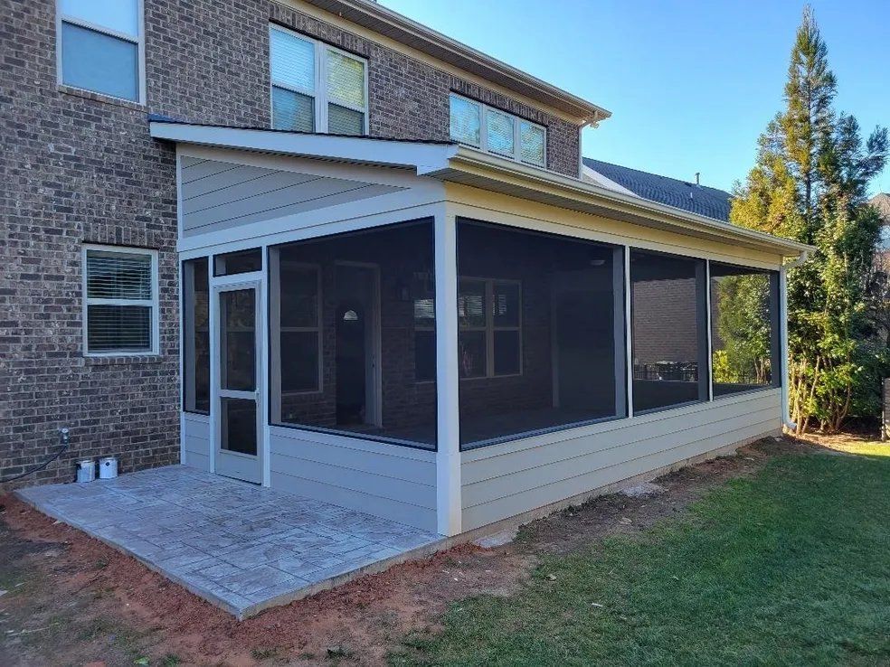 Covered screened porch attached to a brick house with white siding and a concrete patio