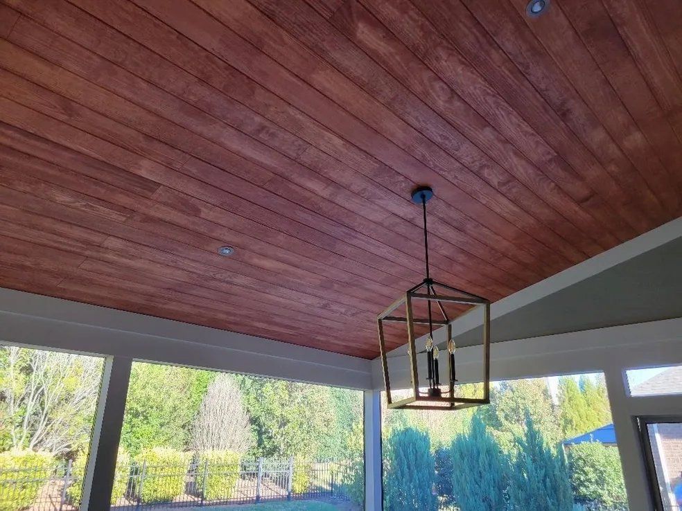 Wood-paneled ceiling with hanging lantern over a bright screened porch and garden view