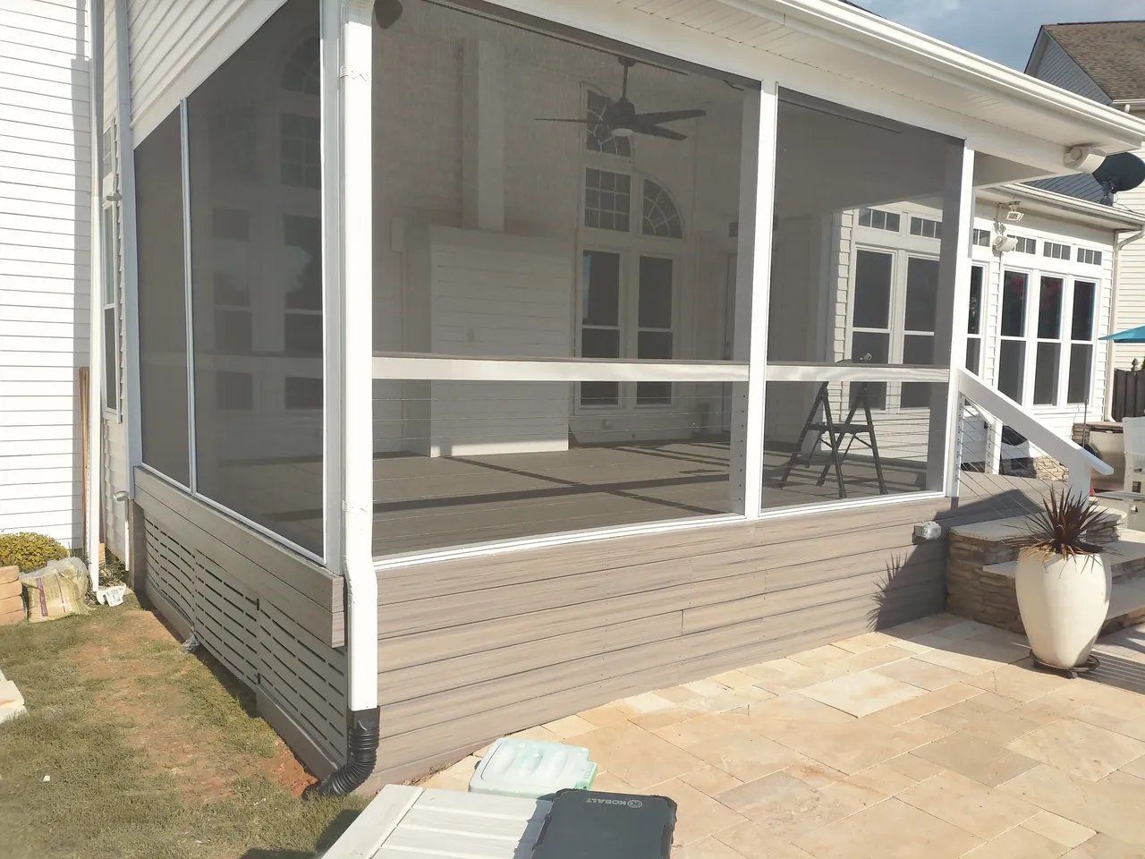 Screened porch with white railing and gray mesh on a concrete patio beside a house