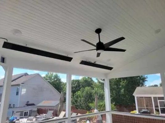Covered porch with a black ceiling fan, white ceiling, and view of neighboring houses and trees.