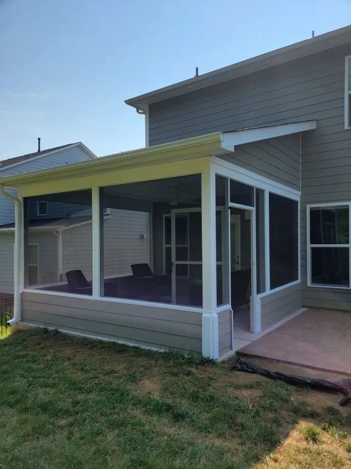 Covered backyard porch with screened sides, yellow roof, and sliding glass door on a house.