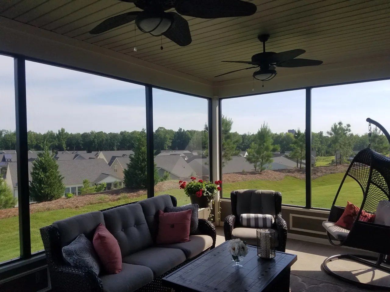 Covered patio with sofa and chairs overlooking a grassy neighborhood and trees at sunset
