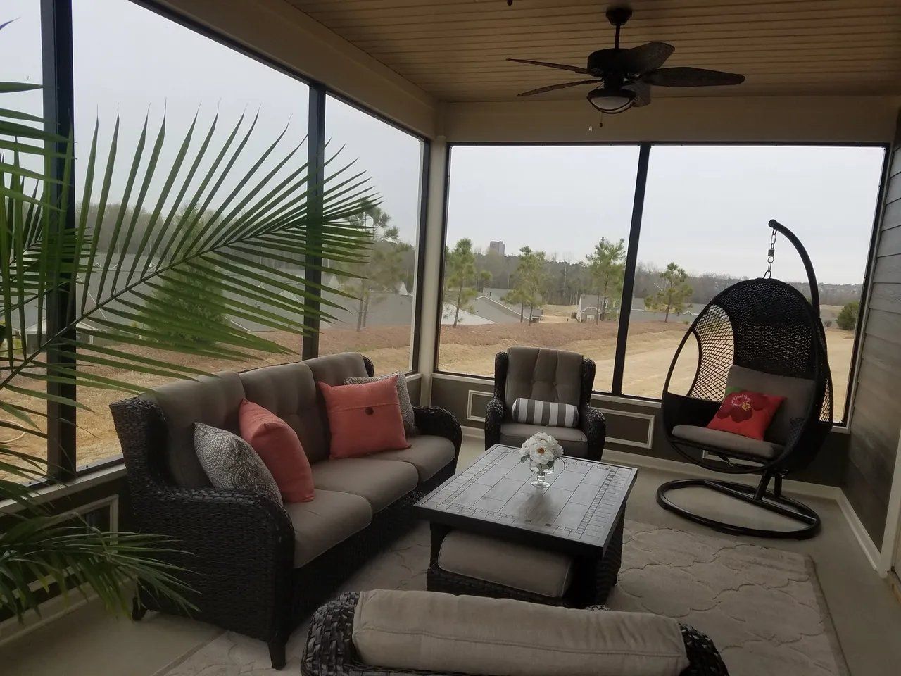Covered patio with wicker seating, cushions, coffee table, and hanging chair overlooking a sandy yard