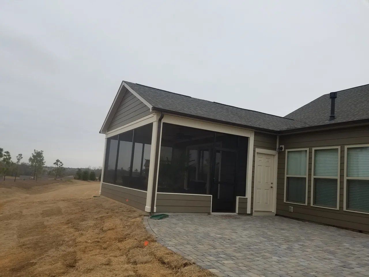 Modern house exterior with screened porch, gray roof, and stone patio beside a dry yard
