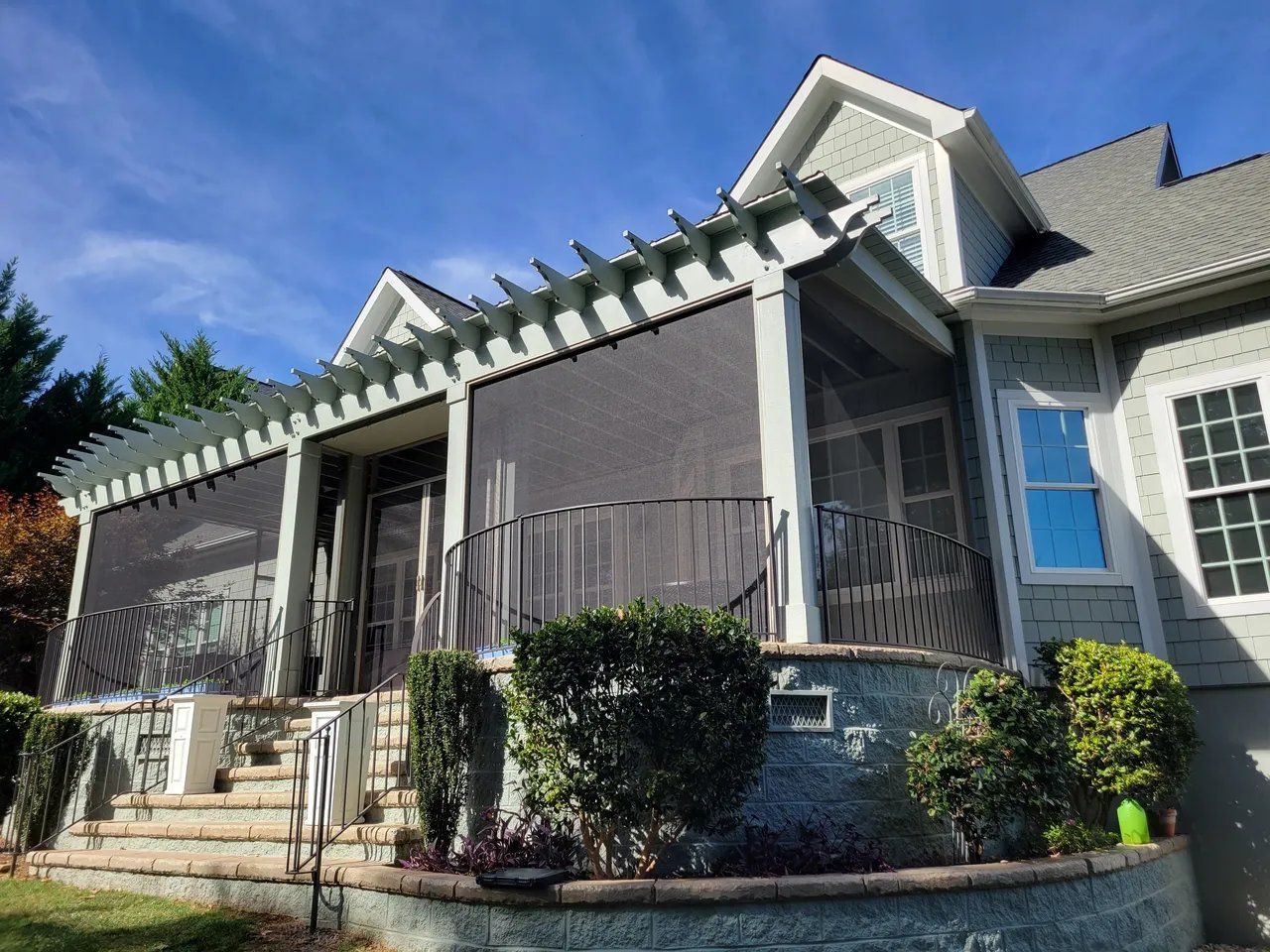 Gray suburban house with white trim, blue window shutters, and a covered front porch with steps and shrubs