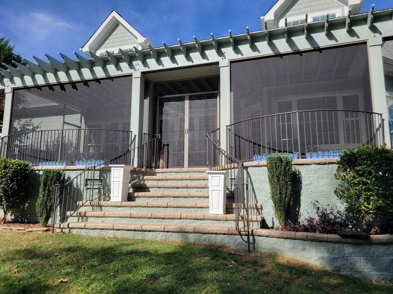 Front porch of a house with steps, black railing, screened windows, and white columns.