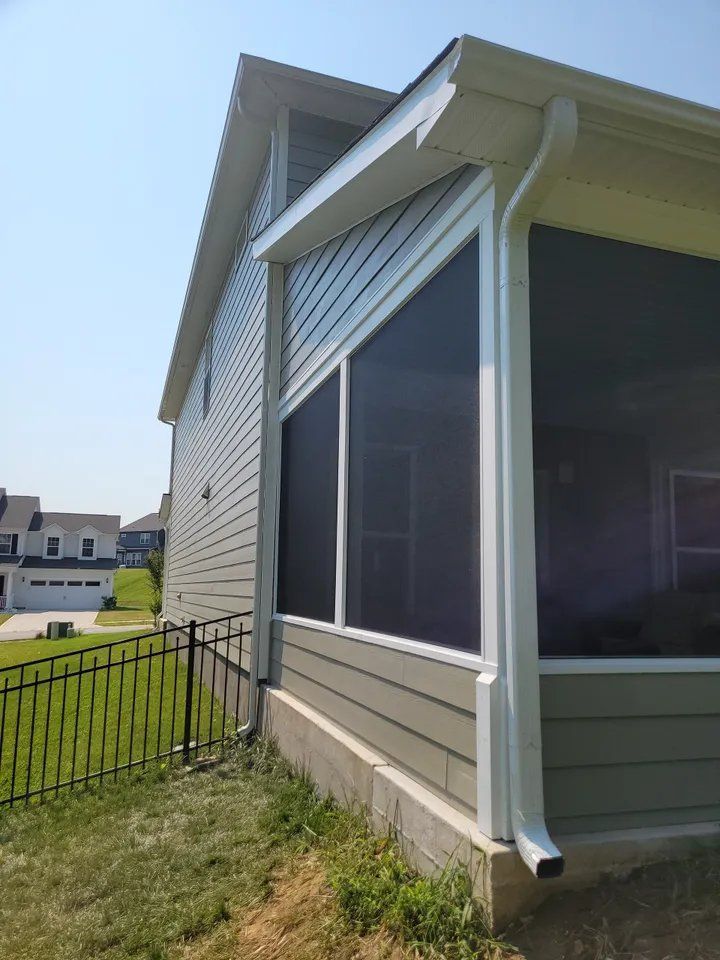 Screened porch with white siding and awning beside a grassy yard and black metal fence