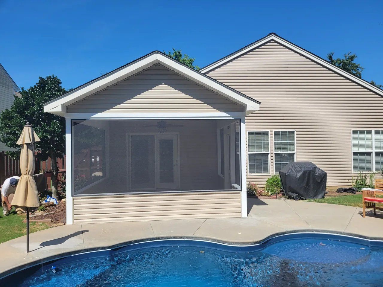 Backyard pool with a screened patio and beige house exterior on a sunny day