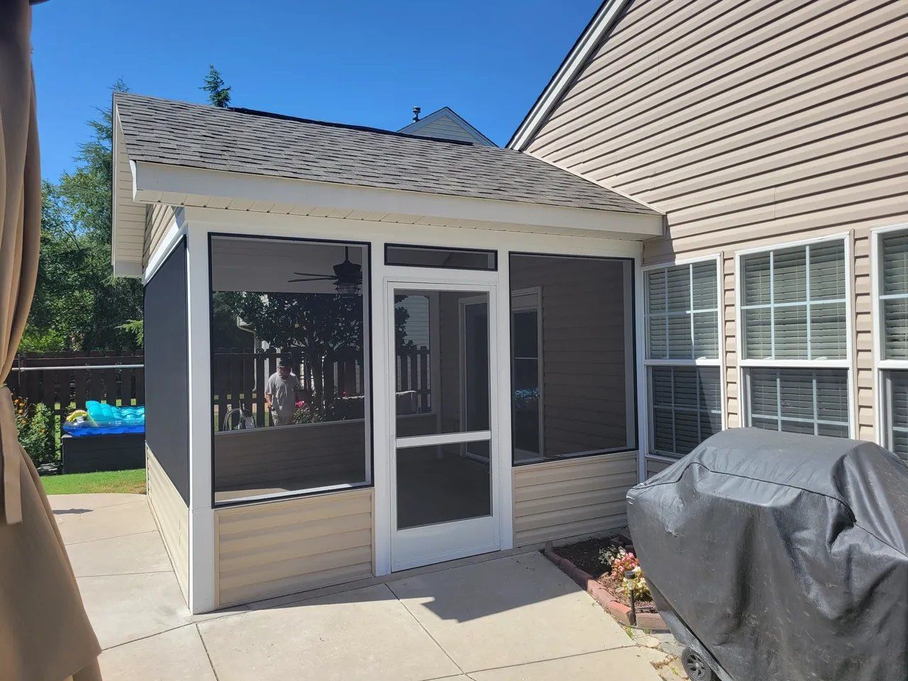 Screened patio enclosure beside a beige house, with a covered grill in the foreground.