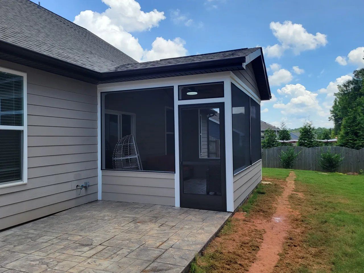 Covered patio beside a beige house with screened porch, concrete slab, and grassy yard under a blue sky