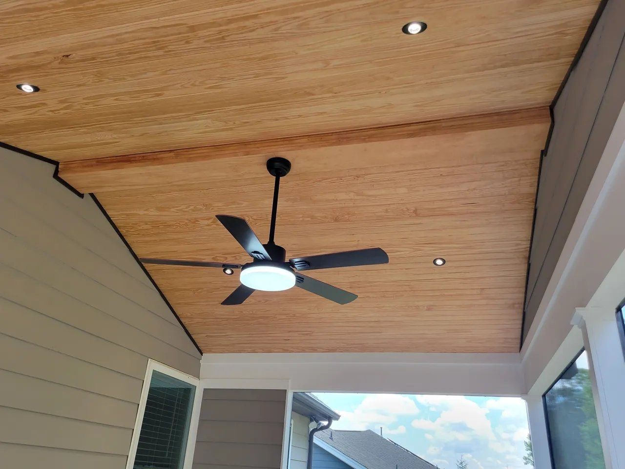 Covered porch ceiling with wood paneling, a black ceiling fan, recessed lights, and house siding below.