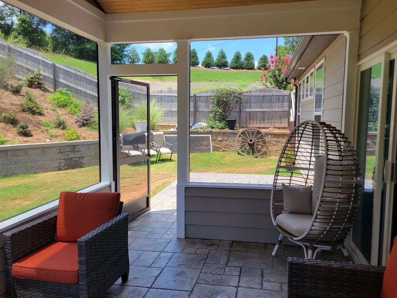 Covered patio with wicker chair, orange cushion, and view of a grassy backyard hillside