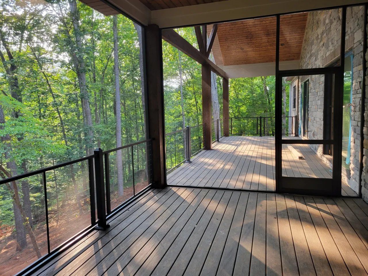Covered wooden deck with black railing and screened porch overlooking a wooded forest.