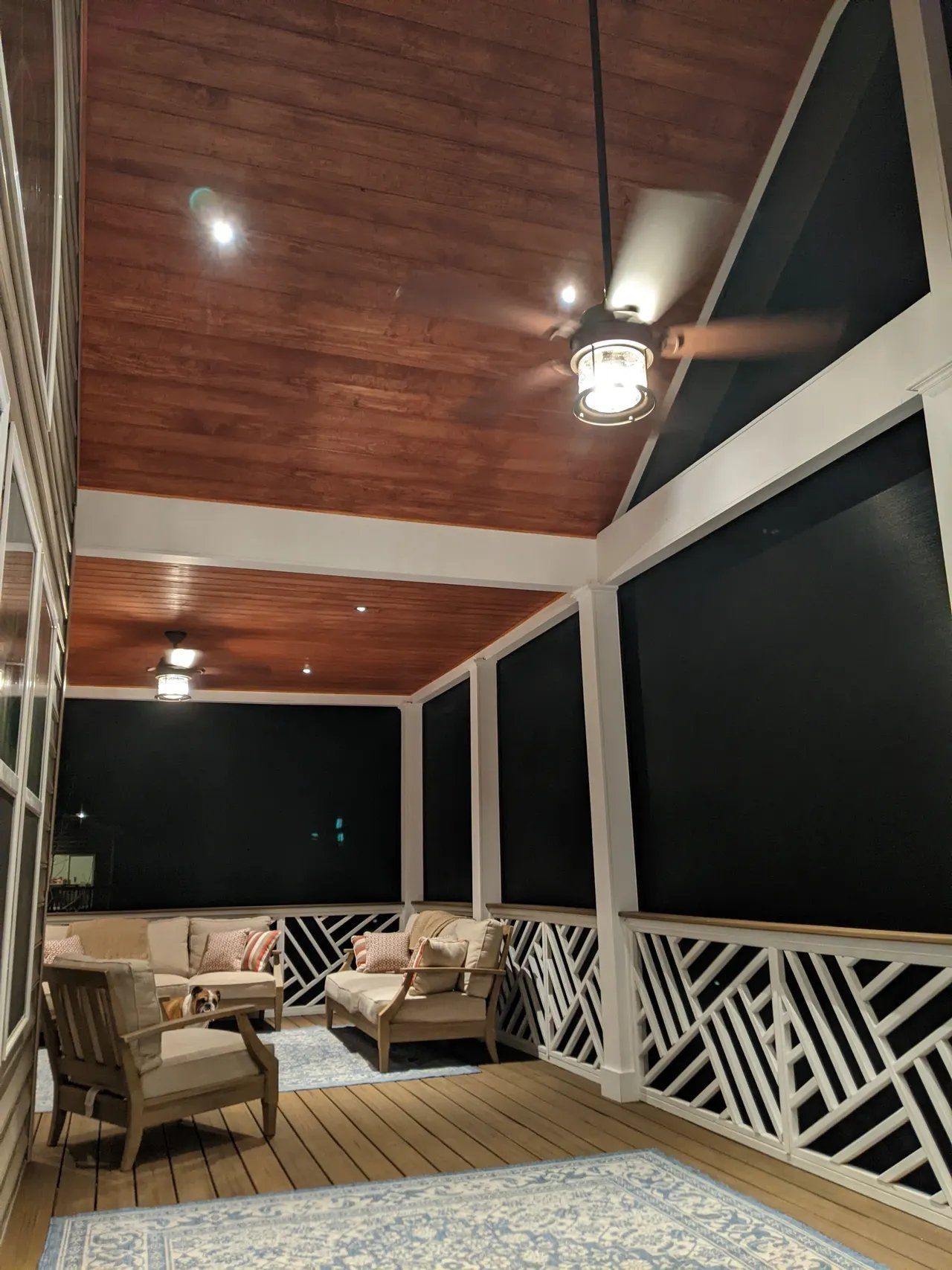 Covered porch with wicker chairs, wooden ceiling, and white lattice railing at night