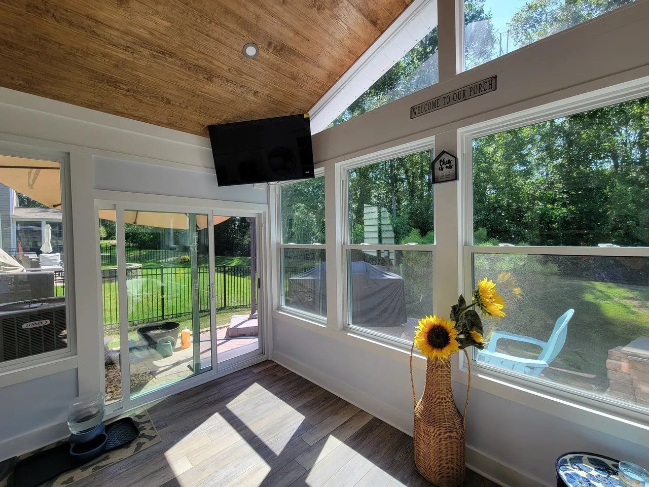 Bright sunroom with wicker vase of sunflowers, white framing, glass walls, and outdoor garden view