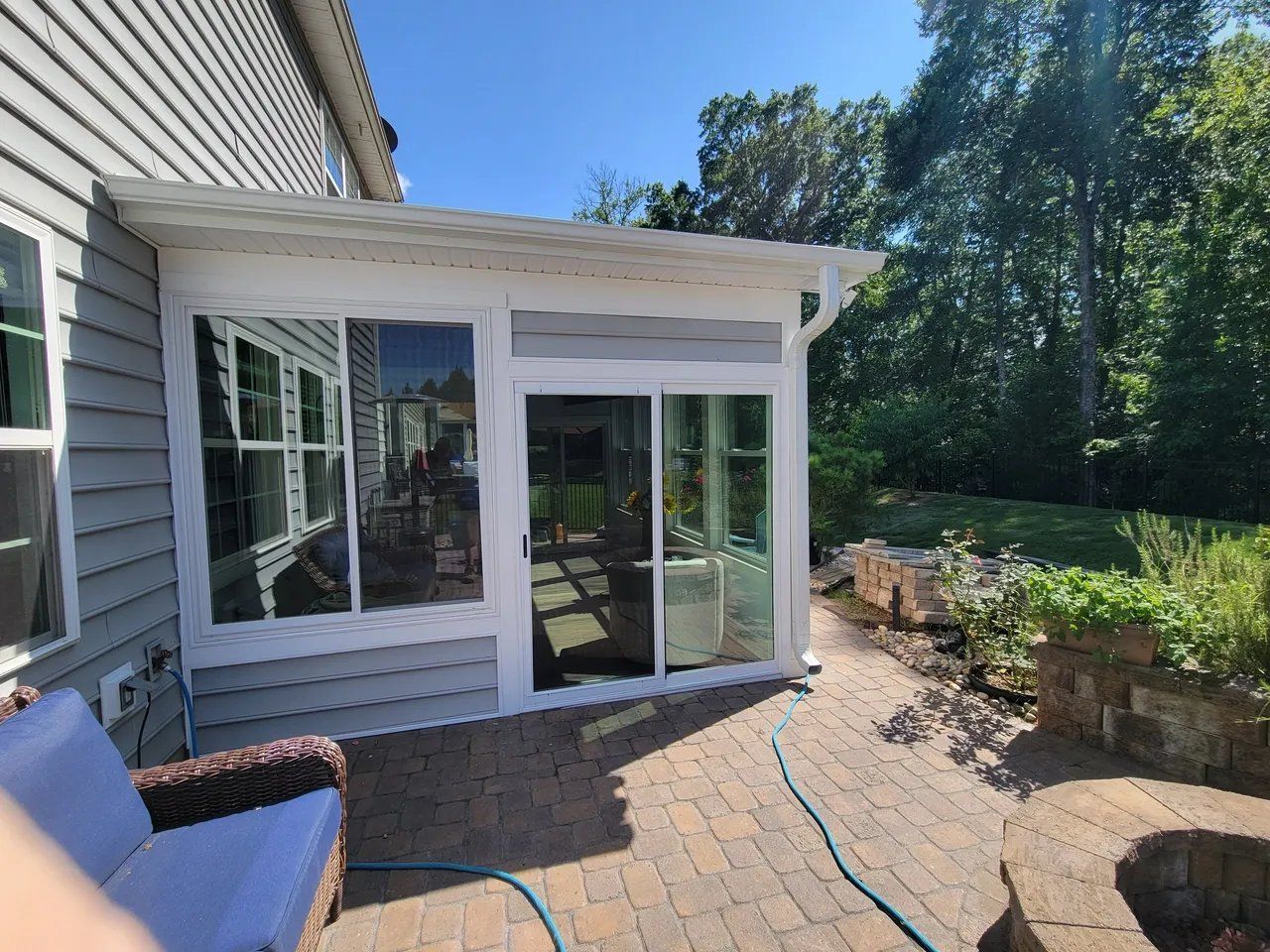 Patio outside a house with sliding glass doors, brick pavers, and a blue chair in sunlight