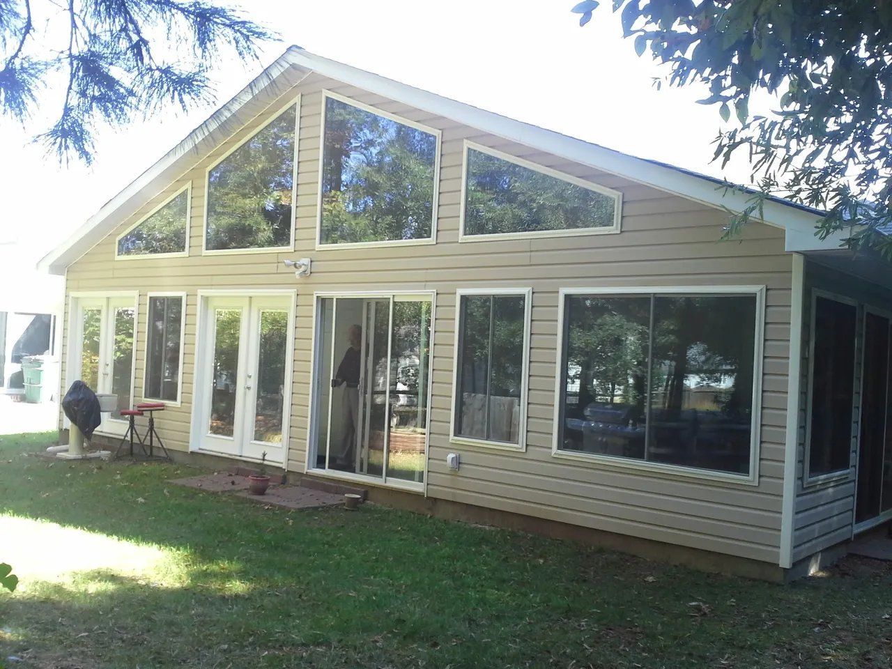 Single-story house with large front windows, beige siding, and a grassy yard in sunlight