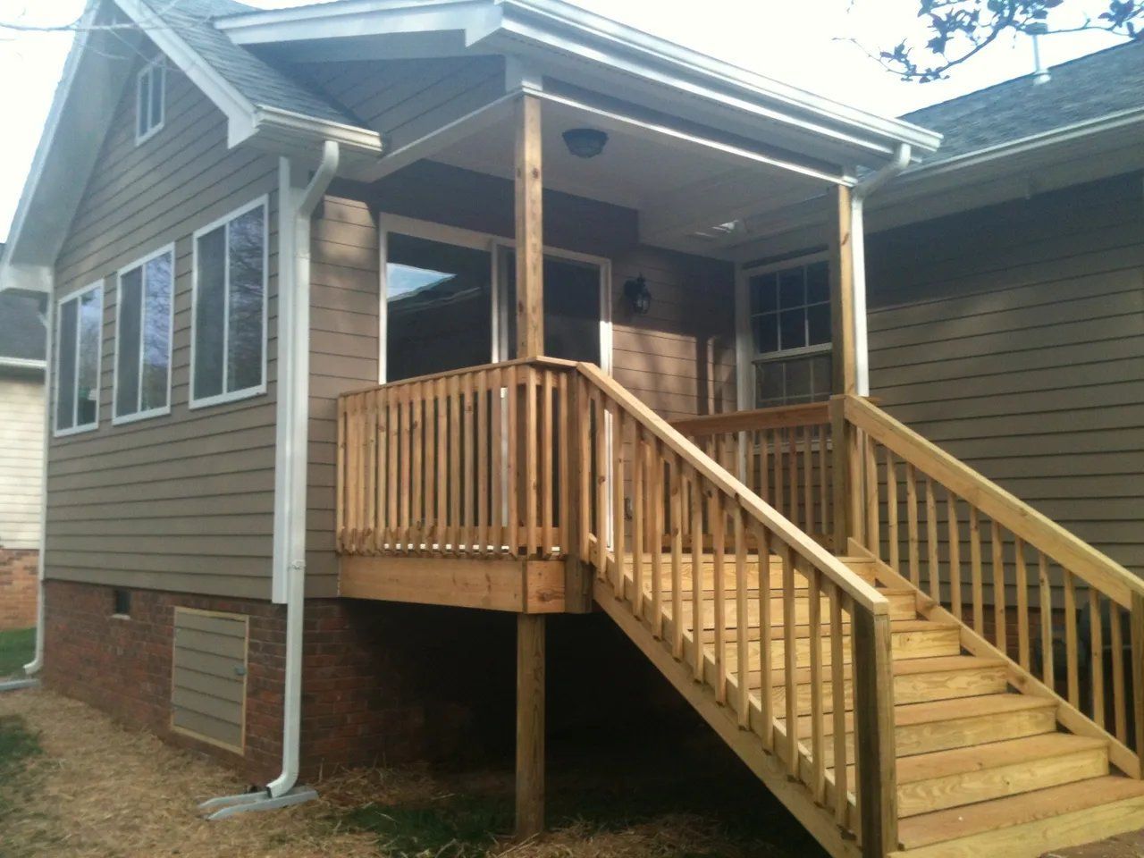 Wooden house porch with ramp and stairs, featuring railings and beige siding