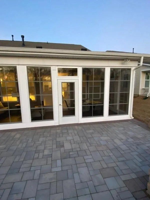 White-framed glass doors and windows opening onto a gray stone patio at dusk