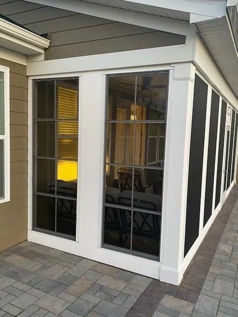 Corner sunroom with white-framed glass windows and gray stone pavers outside
