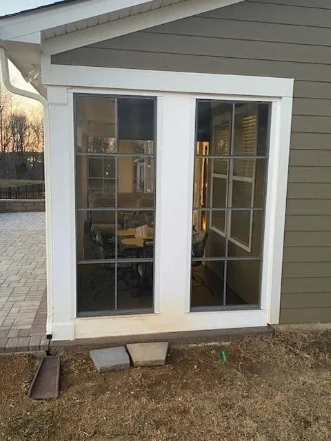 White-framed glass French doors on a house exterior with a small concrete step and dry yard.