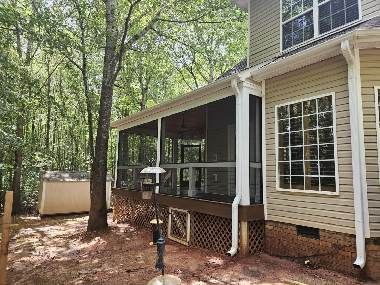 Backyard deck attached to a house, with white railings and trees around it