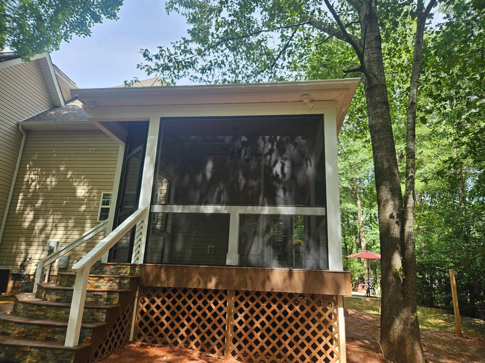 Screened porch with white trim and lattice base on a house surrounded by trees.