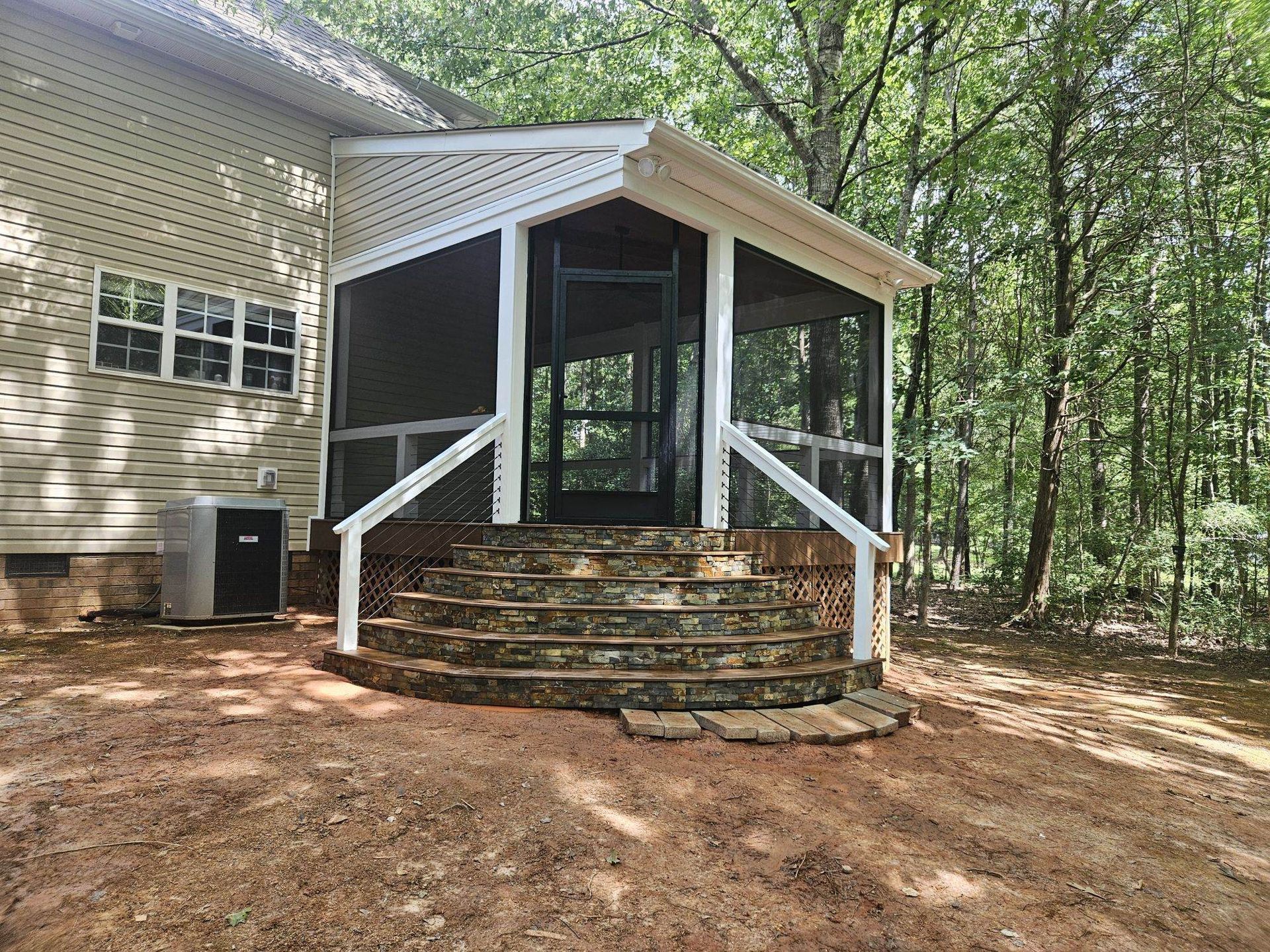 Screened porch with white railings and stone steps on a wooded house exterior
