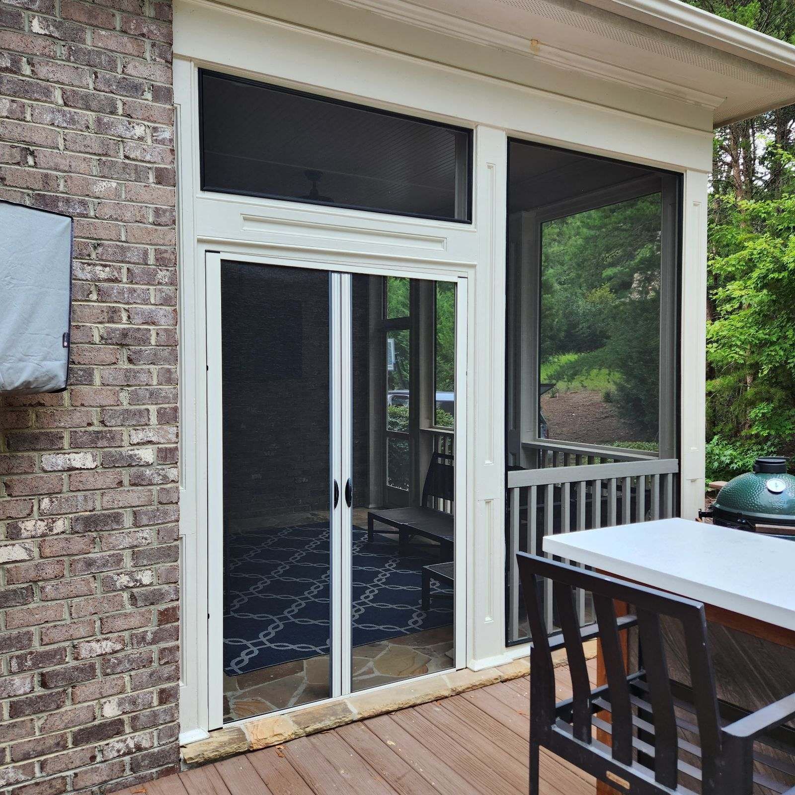 Sliding glass door opening to a porch with brick wall, black railing, and patio table