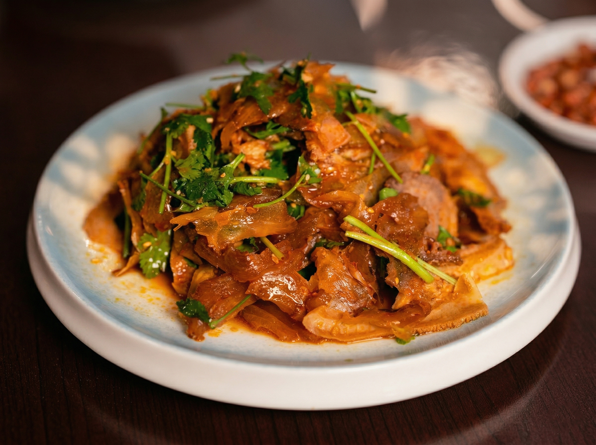A plate of stir-fried sliced meat coated in a savory brown sauce, topped with fresh green cilantro, on a dark table.