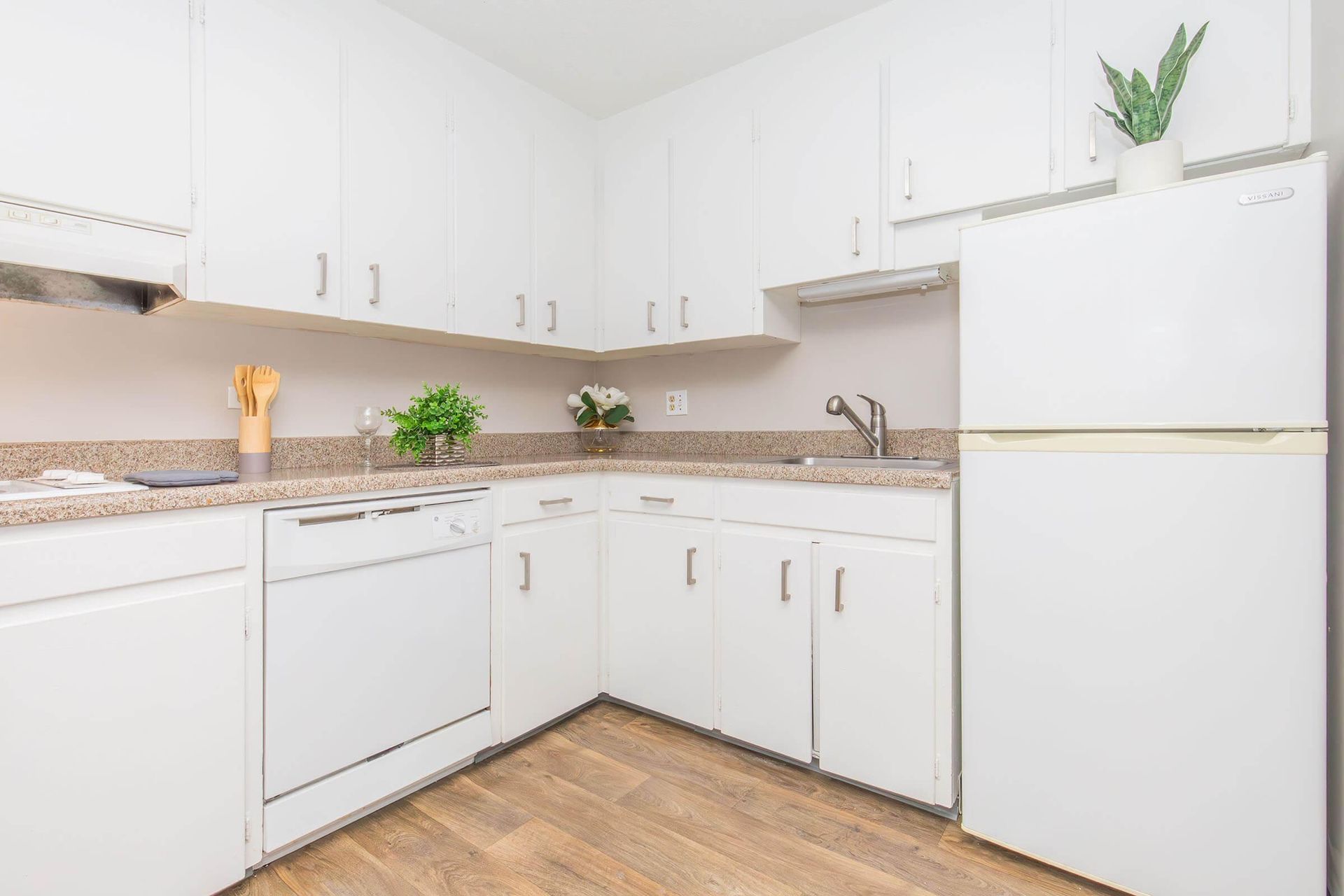 White kitchen with cabinets, appliances, and wooden flooring.