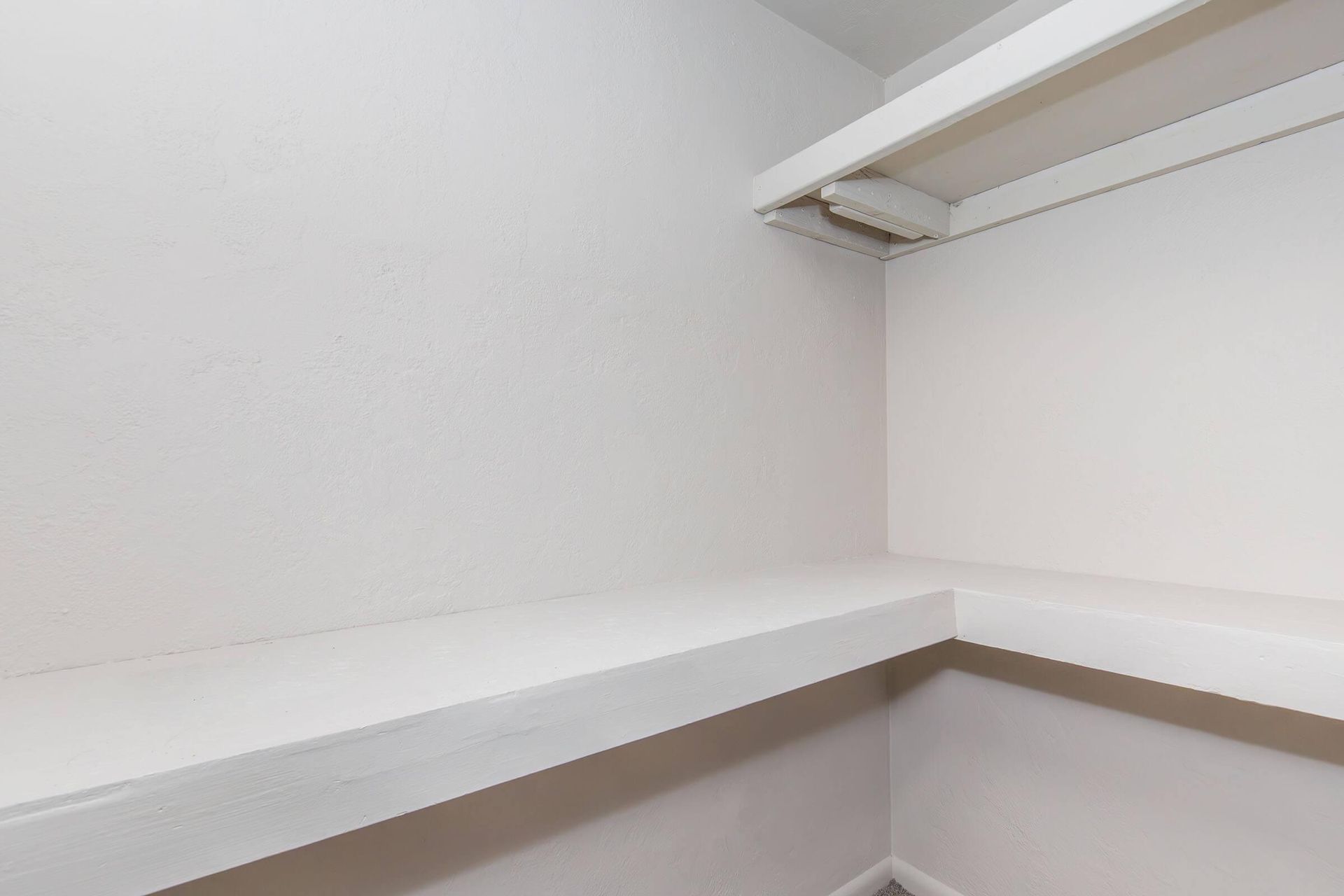 Empty built-in closet with white shelves and walls.