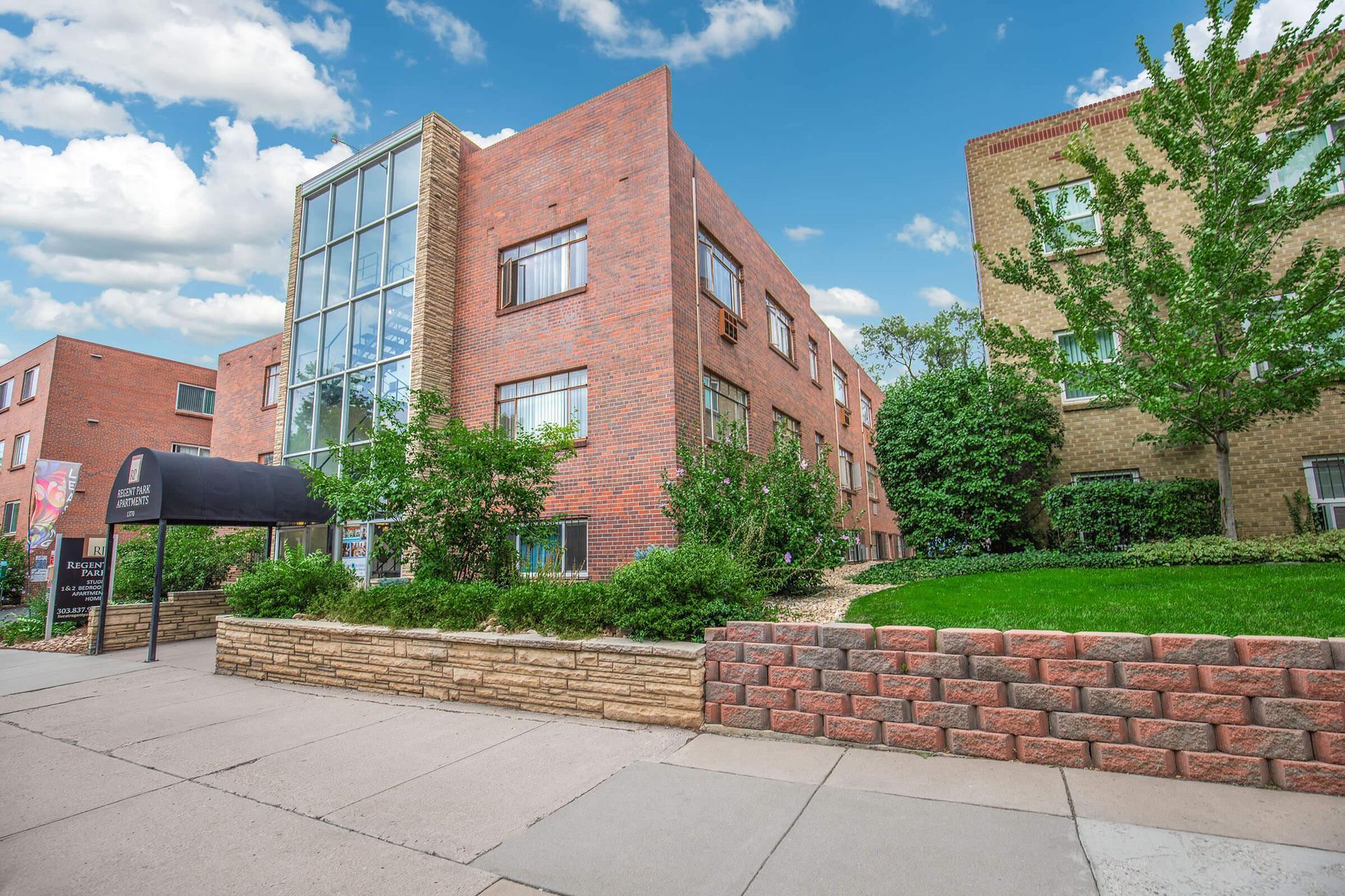 Brick apartment building with glass facade, landscaping, and a blue sky.