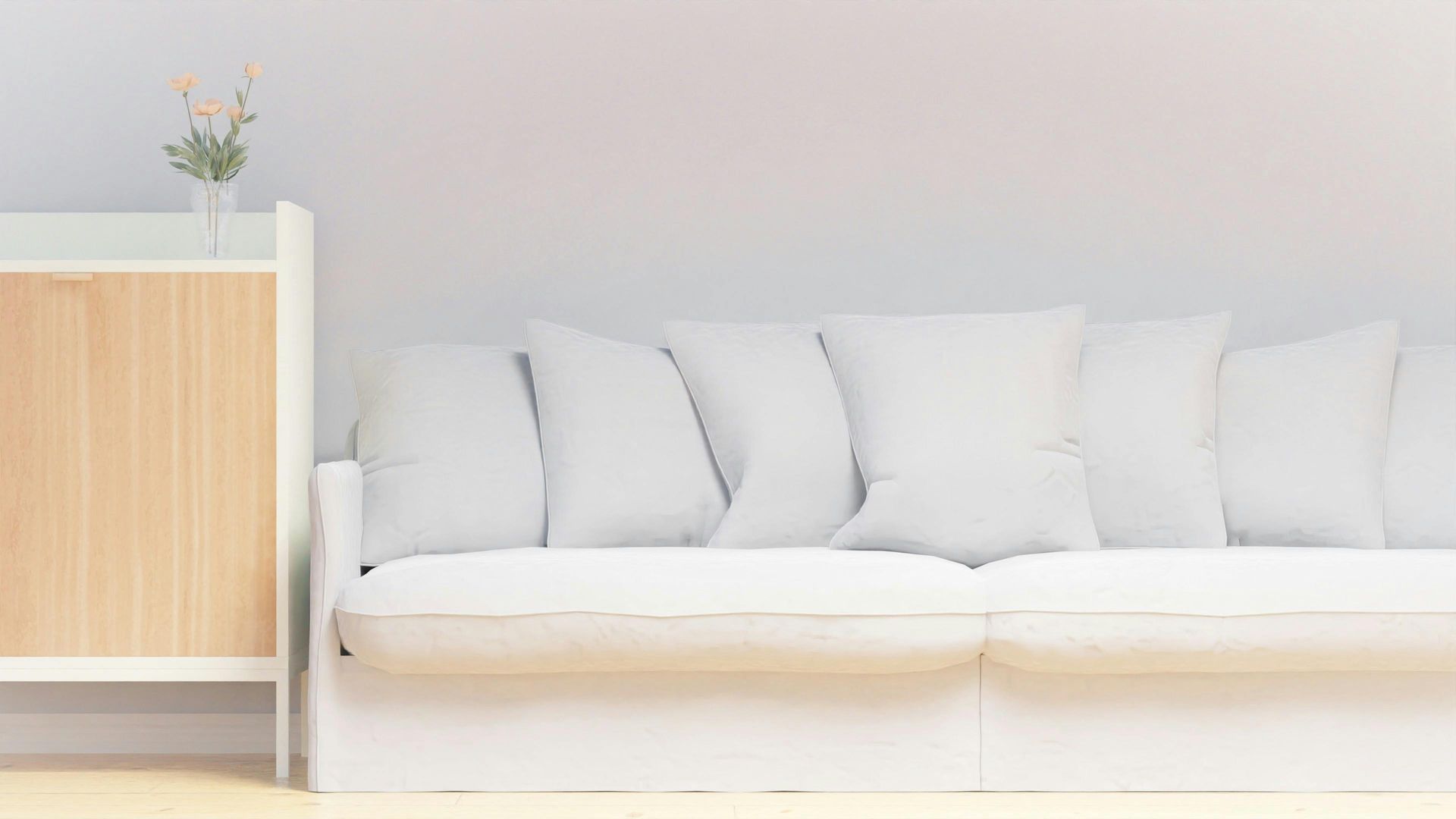 White sofa with pillows next to a light wood cabinet with a vase of flowers.