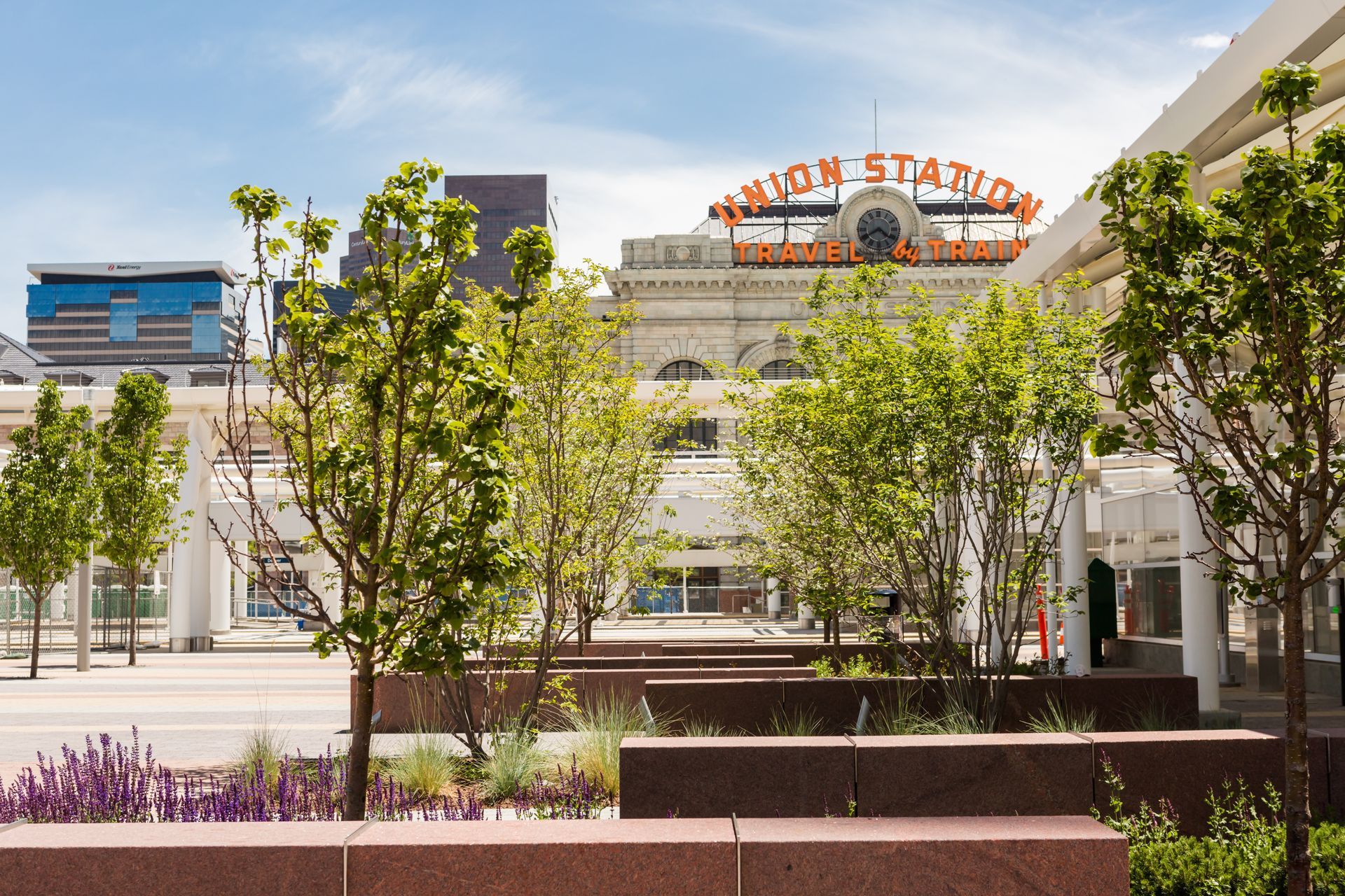 Union Station in Denver, Colorado, seen through trees and a modern plaza on a sunny day.