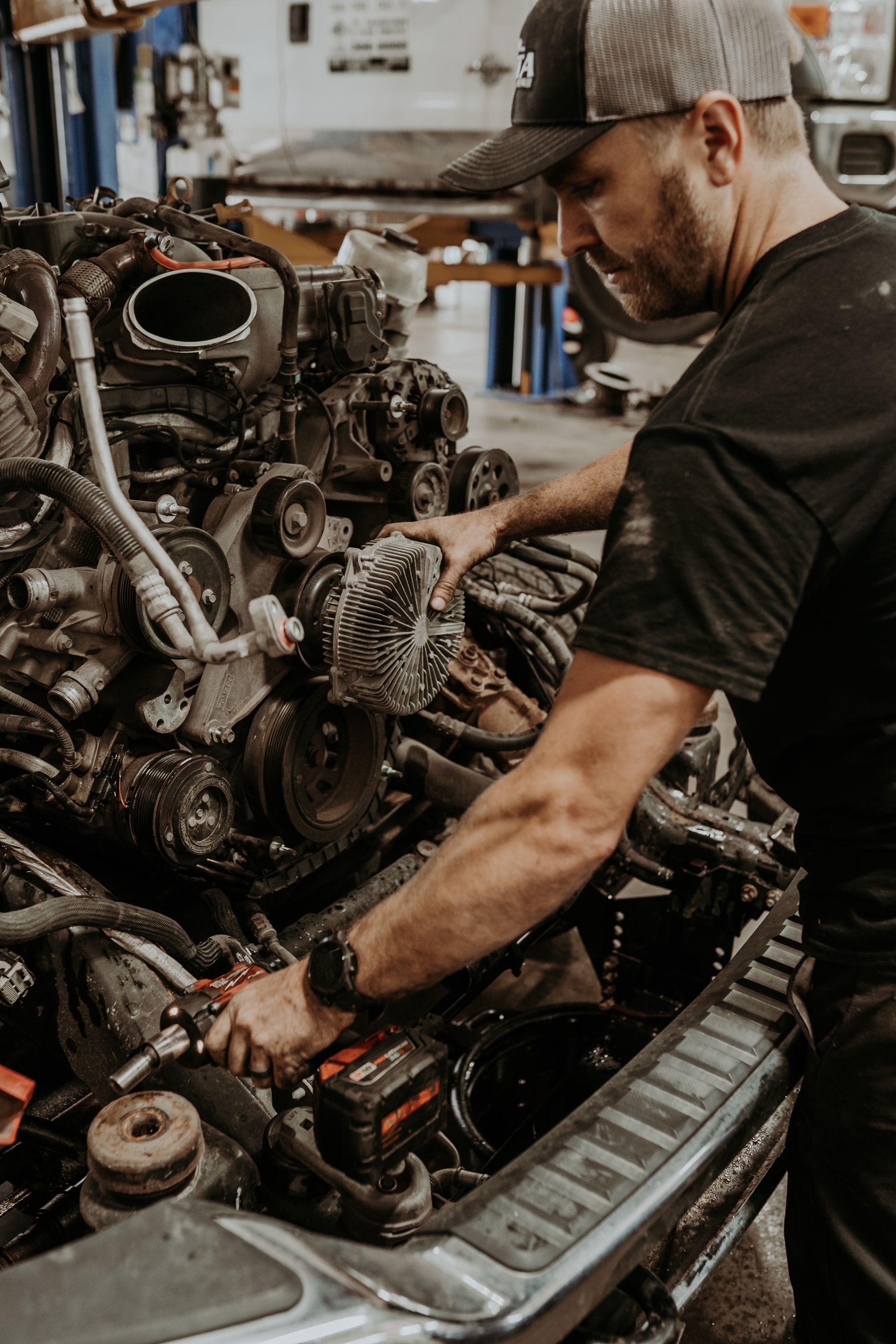 Mechanic works on a car engine, in a garage. Wearing a cap and watch, he holds a wrench | RTA Repair