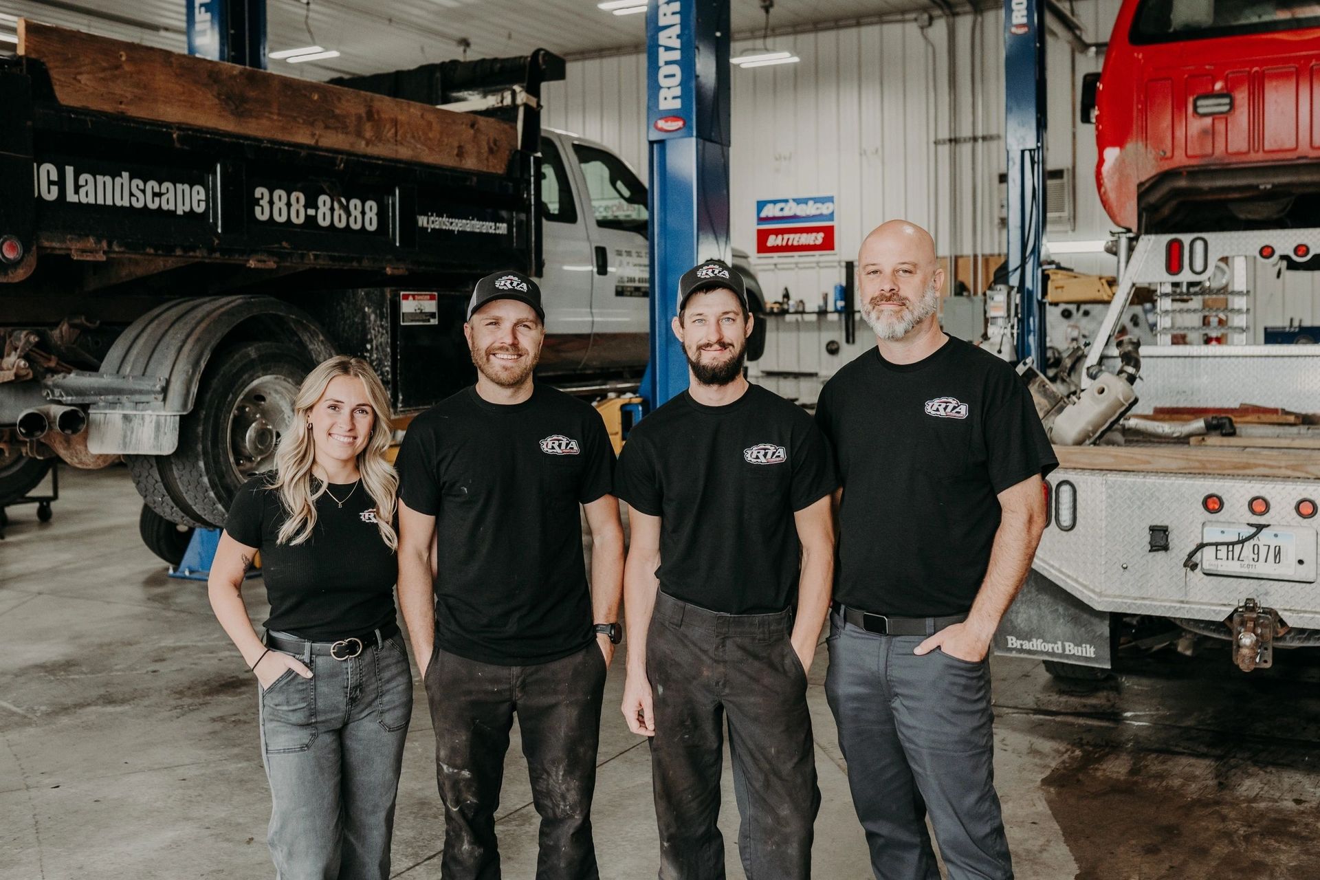 Four people in a garage pose next to a truck. Two people in black shirts, one person in gray pants, and one with a bald head | RTA Repair