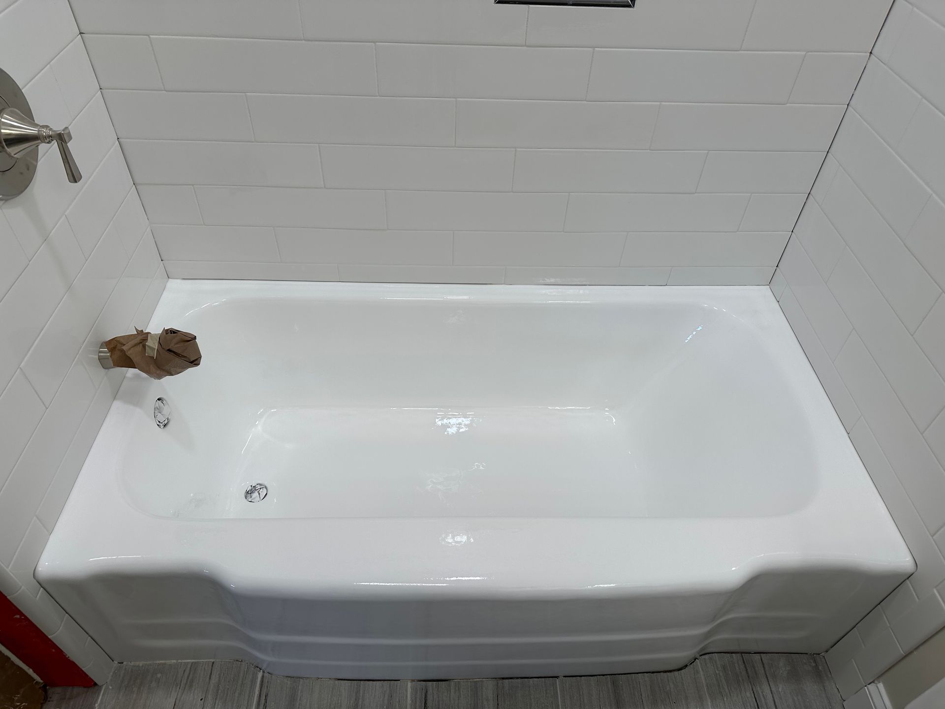 A white bathtub is sitting in a bathroom next to a white tiled wall.