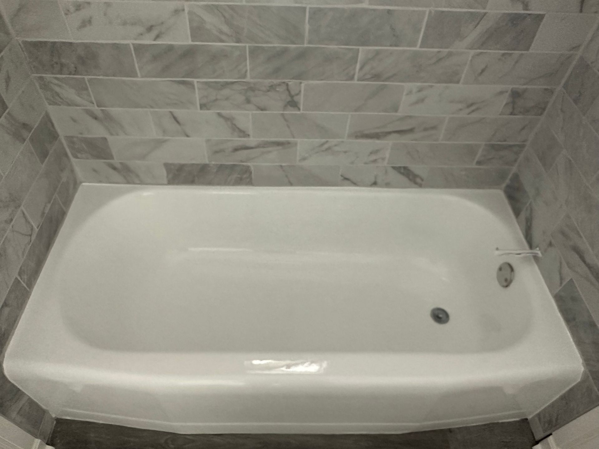 A white bathtub is sitting in a bathroom next to a white tiled wall.