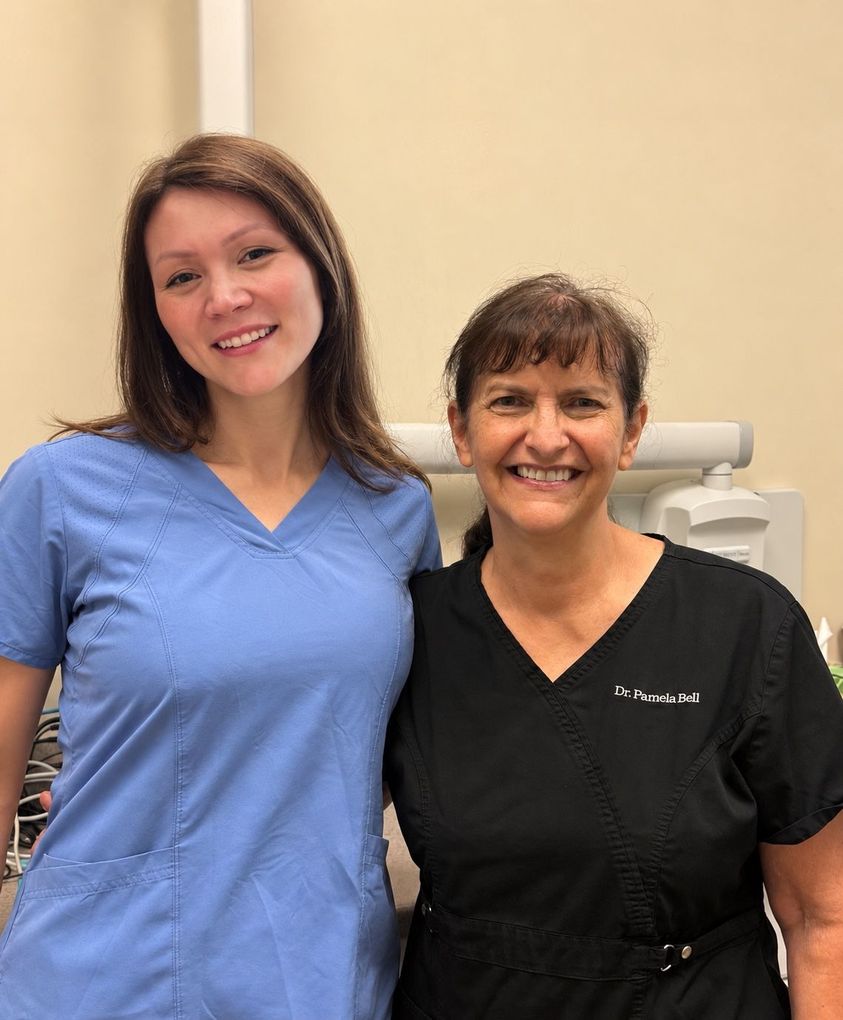 Two smiling medical staff in blue and black scrubs standing in a clinic room