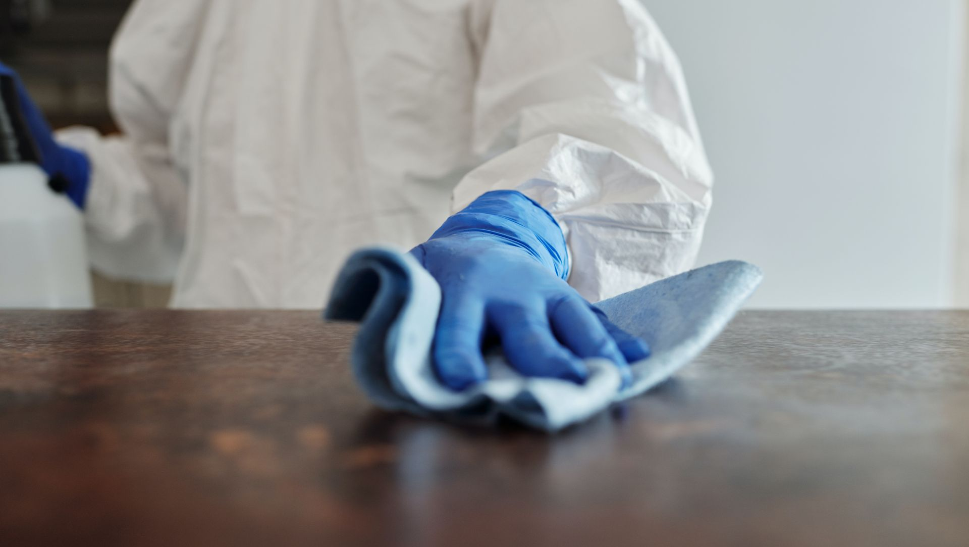 Blue-gloved hand wiping a wooden table with a cloth during cleaning