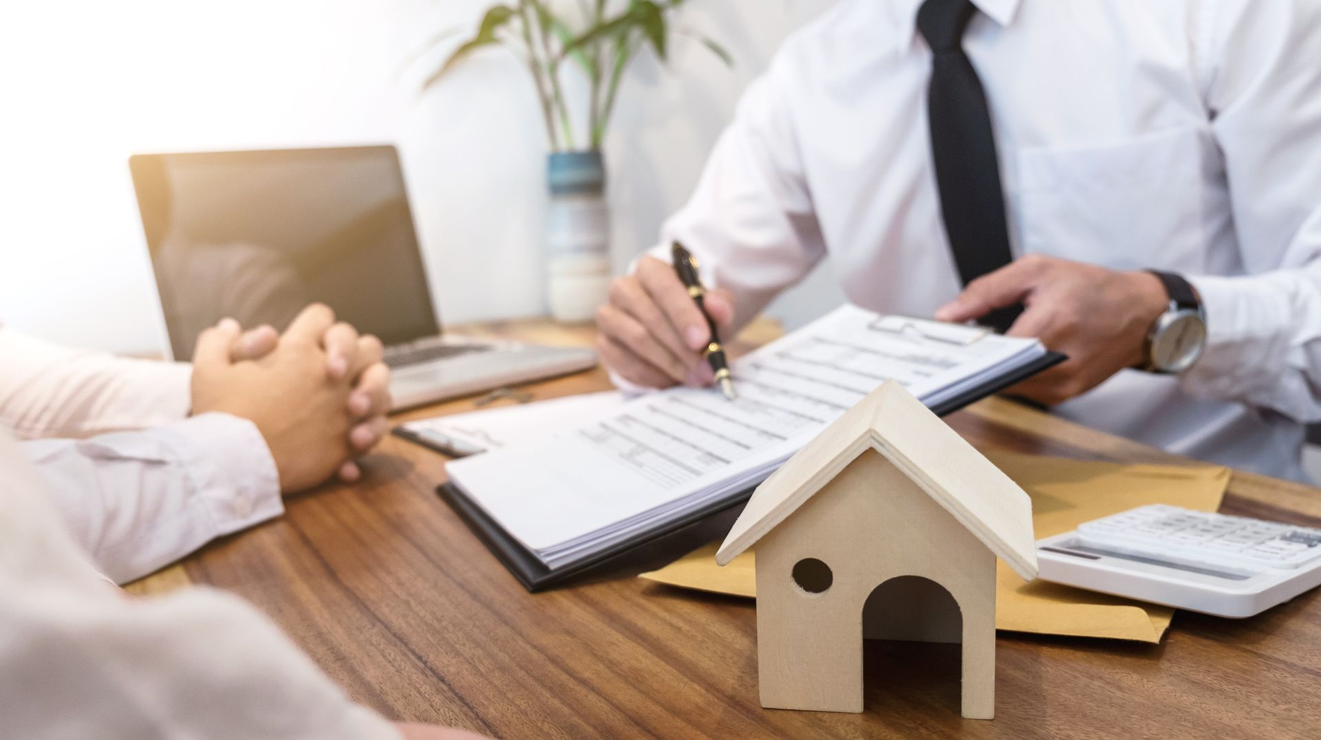 Person signing real estate documents; miniature house on table.
