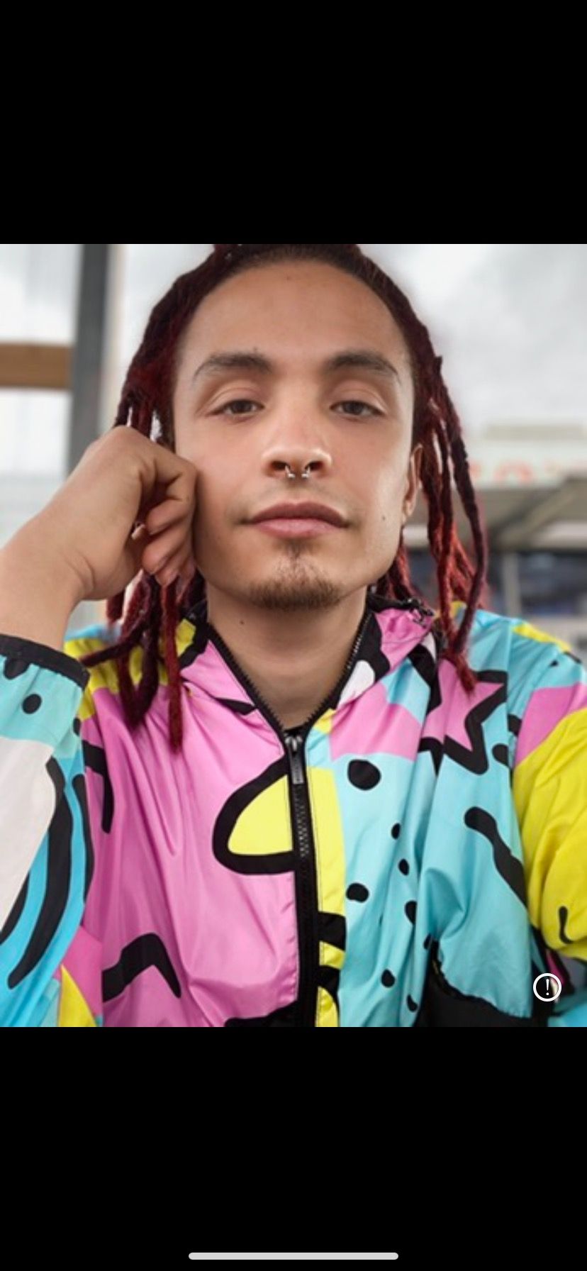 A man with dreadlocks is wearing a colorful jacket.