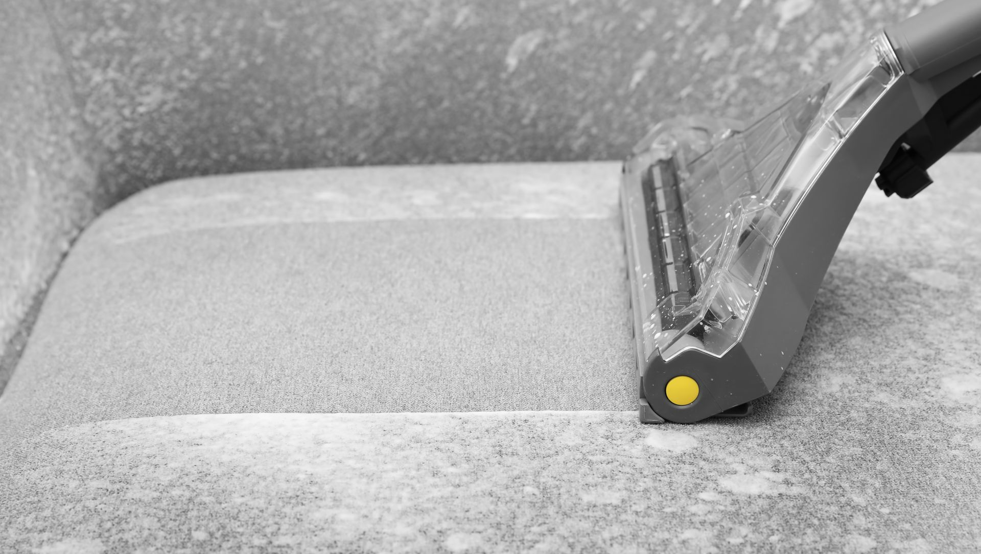 Yellow clamp on a gray textured surface, securing a plastic edge in a close-up view.