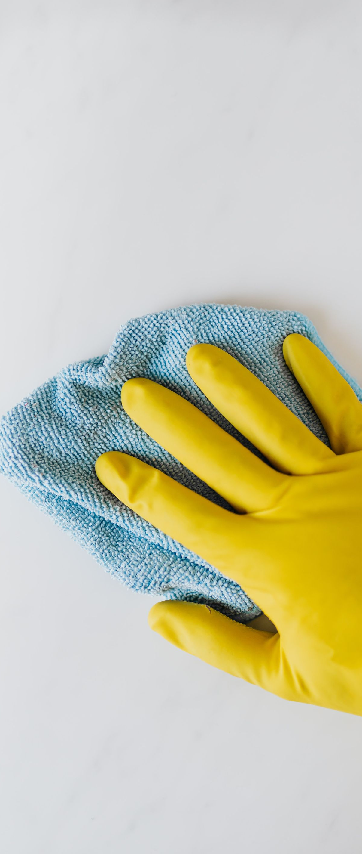 Yellow rubber-gloved hand wiping a white surface with a blue cleaning cloth.